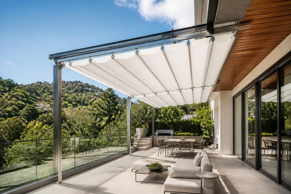Retractable awning folded up against a house exterior over a patio with a glass railing.